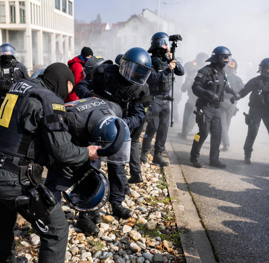 A police officer hit by a powder extinguisher is treated by two other police officers during a demonstration against the state party conference of the AfD Baden-Württemberg